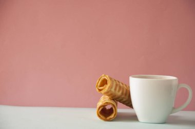 Yumuşak pembe arka planda yuvarlanan beyaz kahve fincanı.