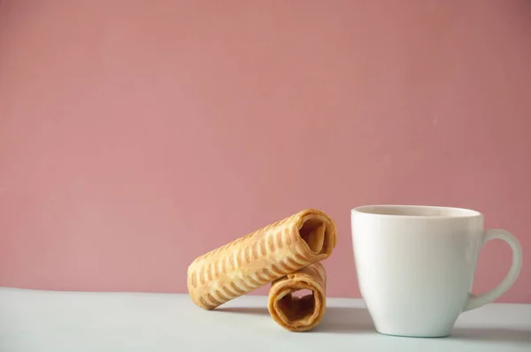 Біла чашка кави з вафельними рулонами на м'якому рожевому фоні — стокове фото