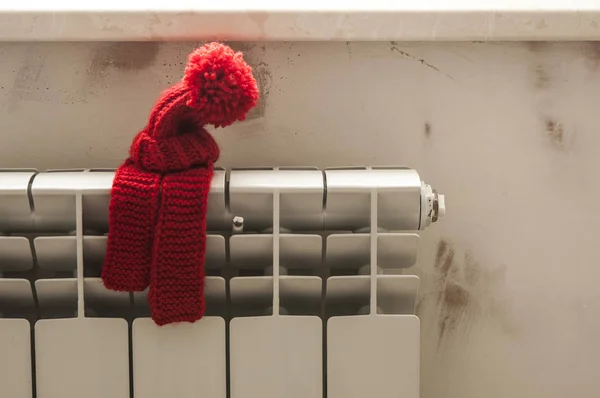 暖气散热器上戴着红色针织帽子和围巾的房子模型. — 图库照片