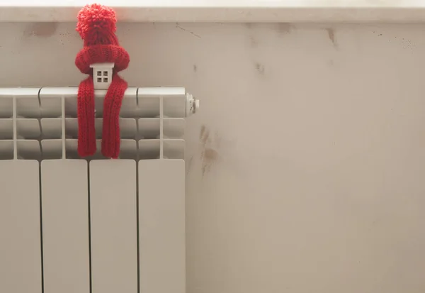 Modello casa con cappello a maglia rossa e sciarpa sul radiatore di riscaldamento . — Foto Stock