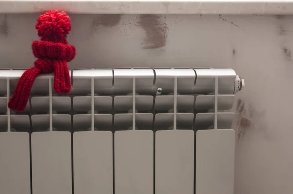 Modèle de maison avec chapeau tricoté rouge et écharpe sur radiateur de chauffage . — Photo