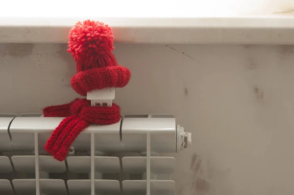 Modelo de casa con sombrero de punto rojo y bufanda en radiador de calefacción . —  Fotos de Stock