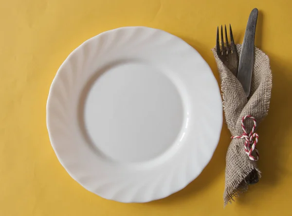 White plate, knife and fork at napkin on yellow paper  backgroun — Stock Photo, Image