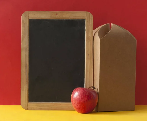 Braune Papiertüte und ein roter Apfel auf buntem Papier Hintergrund — Stockfoto