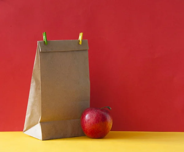 Brązowa papierowa torba i czerwone jabłko na kolorowym papierowym tle — Zdjęcie stockowe