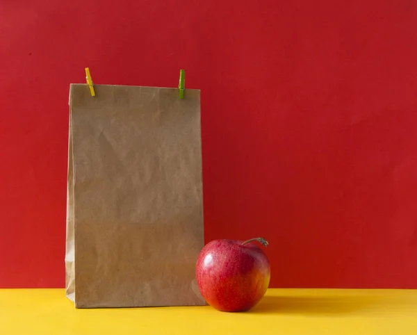 Braune Papiertüte und ein roter Apfel auf buntem Papier Hintergrund — Stockfoto