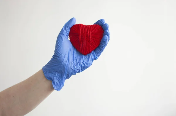 En hand i en blå handske håller ett rött hjärta. Medicinskt koncept. Uppfattat. — Stockfoto