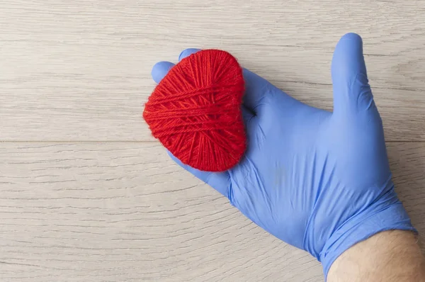 En hand i en blå handske håller ett rött hjärta. Medicinskt koncept. Uppfattat. — Stockfoto