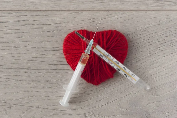 An old mercury thermometer with syringe and red heart on wood ba