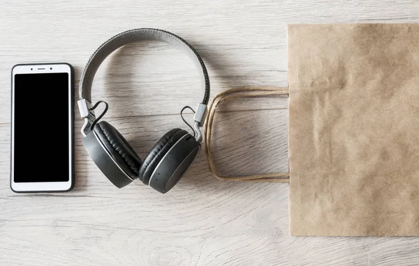 Headphones, smartphone and brown paper bag on wooden table. Top — Stock Photo, Image