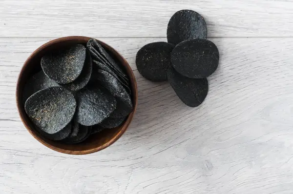 Schwarze Kartoffelchips in Holzschüssel auf Holztisch. — Stockfoto