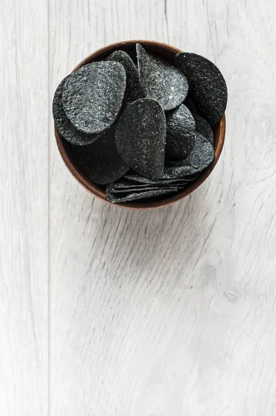 Batatas fritas pretas em tigela de madeira na mesa de madeira . — Fotografia de Stock