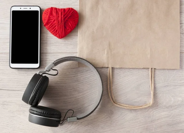 headphones, smartphone and brown paper bag on wooden table. Top