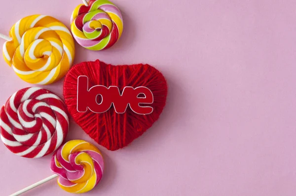 Amor palabra, corazón y caramelos de piruleta sobre fondo de papel rosa . —  Fotos de Stock