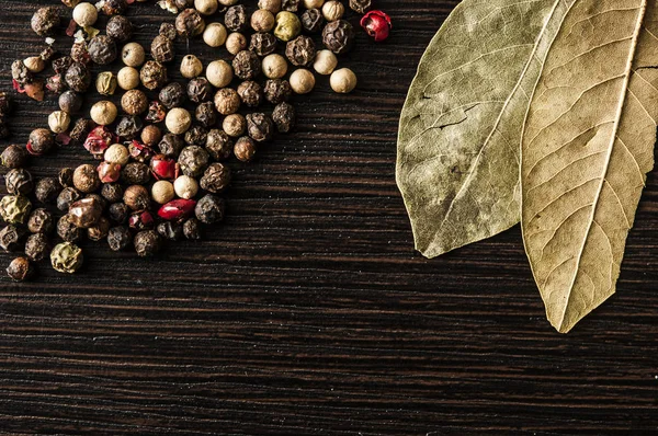 Bay leaf on a black background with black pepper peas — Stock Photo, Image
