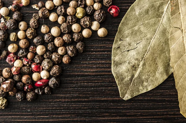 Bay leaf on a black background with black pepper peas — Stock Photo, Image