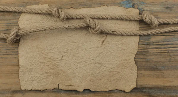 铺在木板上的一张旧羊皮纸或一张旧纸片 一根粗糙的绳子拉成一个航海结 形成一个框架 — 图库照片