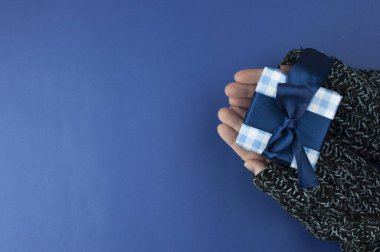 Hediye paketlenmiş ve süslenmiş, mavi arka planda fotokopi alanı ile süslenmiş kadınların düz uzanmış elleri.