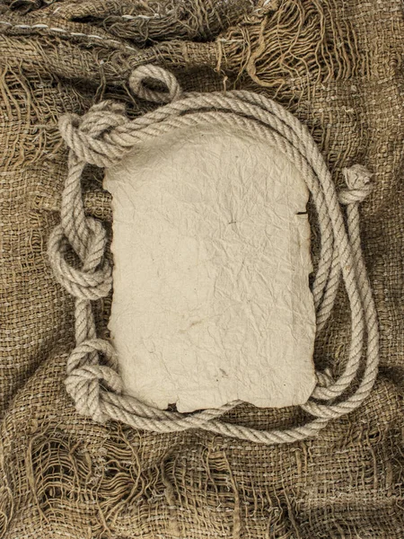 Hemp rope with vintage torn paper on burlap background. Close-up of a natural rope and fabric. Put your own text here