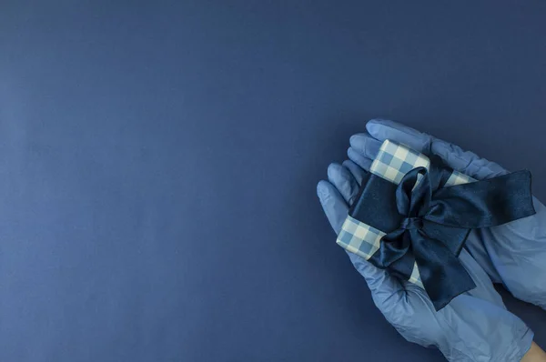 青い医療用手袋の女性の手は 上にギフトボックスを保持しています 青い背景にコピースペースとウイルスやコロナウイルス検疫で安全メール商品宅配便の概念 — ストック写真