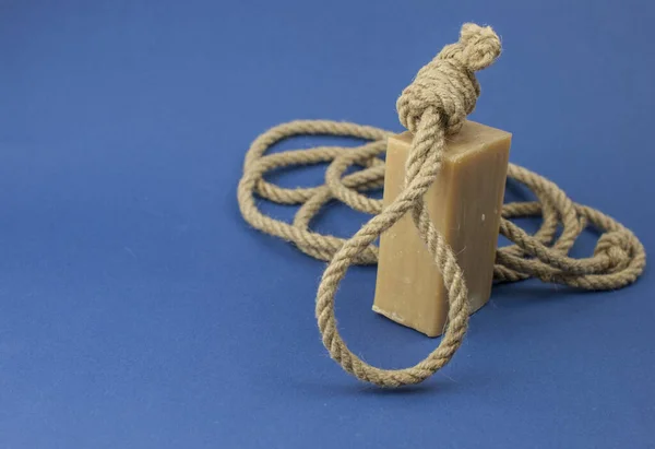 Rope with loop and brown soap on blue background. Rope with hangman\'s noose. Suicide concept