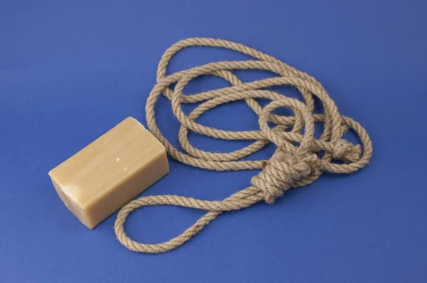 Rope with loop and brown soap on blue background. Rope with hangman's noose. Suicide concept