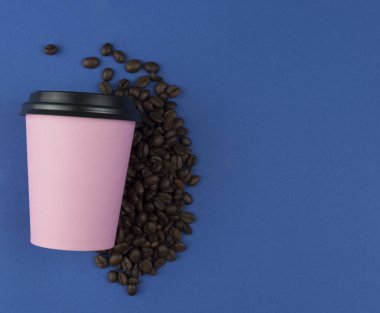 Kahve çekirdekli mavi arka planda plastik kapaklı pembe kağıt kahve fincanı. Kahve fincanı ve paket kahve. Kopyalama alanı, düz uzanma.