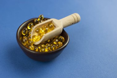 Morina ciğeri yağı omega 3 jel kapsülleri mavi kağıt arka planda ahşap kaşık