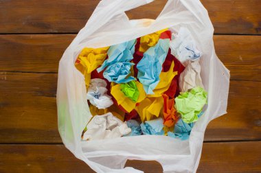 Çöp torbası plastik, ahşap zeminde renkli buruşuk kağıtlar.