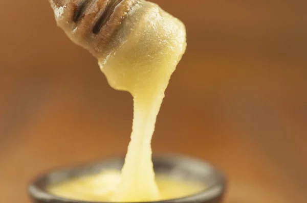 Honey dripping from honey dipper in clay bowl. Close-up. Healthy organic Thick honey dipping from the wooden honey spoon, closeup. Sweet dessert background