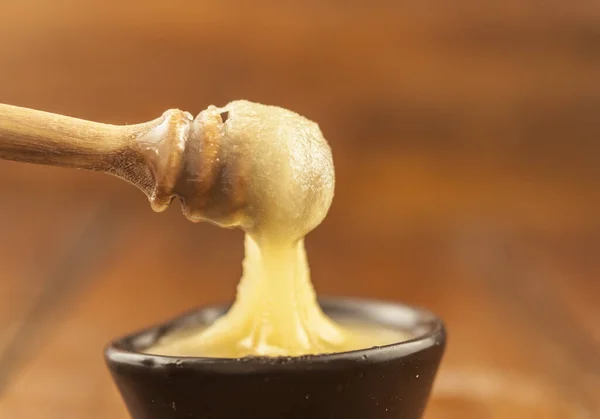 Honey dripping from honey dipper in clay bowl. Close-up. Healthy organic Thick honey dipping from the wooden honey spoon, closeup. Sweet dessert background