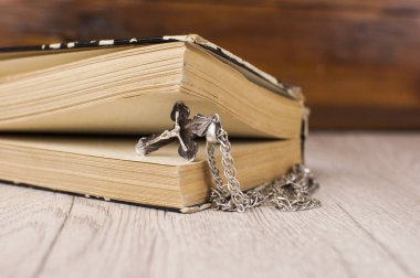 Gümüş zincirli, ahşap arka planlı, boş bir kitapla Hıristiyan haçı kapatıldı.