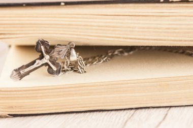 Gümüş zincirli, ahşap arka planlı, boş bir kitapla Hıristiyan haçı kapatıldı.