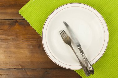 Tahta arka planda çatal bıçak takımı olan beyaz tabak.