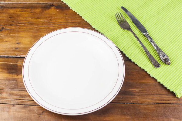 White plate with cutlery on wooden background