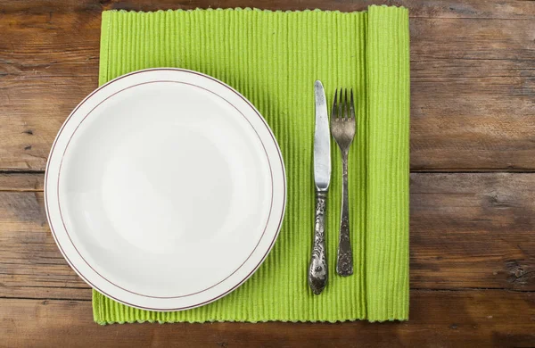 Tahta arka planda çatal bıçak takımı olan beyaz tabak.