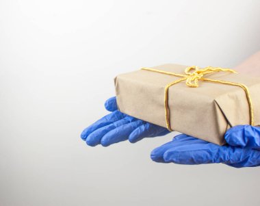 Mavi, tek kullanımlık bir eldivende beyaz arka planda bir fiyonk olan hediye kutusu bulunur.