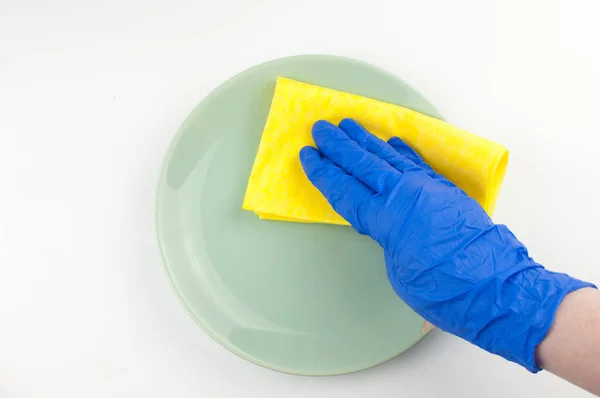 蓝色手套手中的一个空的绿色盘子 白色背景上有一块黄色的破布 — 图库照片