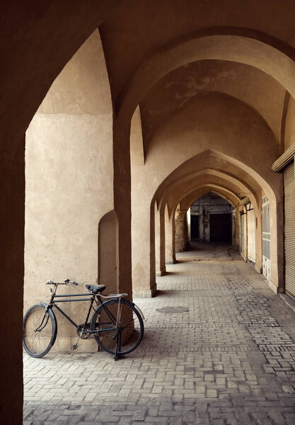 Велосипед припаркован в традиционном проходе с глинистыми арками в городе Язд
