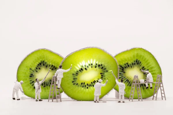 Miniature painters coloring Kiwi slices. Macro photo — Stock Photo, Image