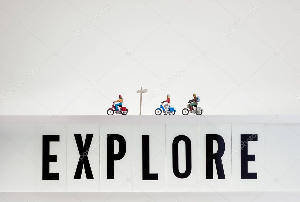 Miniature travellers ride over lightbox with the word Explore
