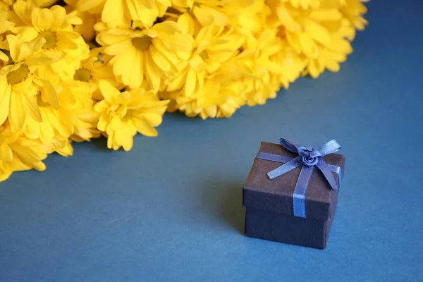 a surprise gift with a bouquet. Gift box on a blue background with yellow flowers .