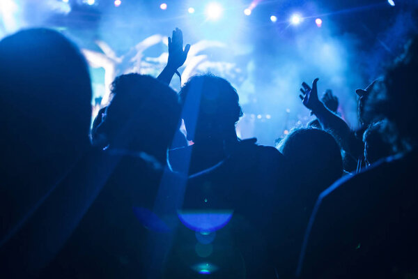 Photo of many people enjoying concert, crowd with raised up hands dancing in nightclub, audience applauding to musician band, night entertainment, music festival.