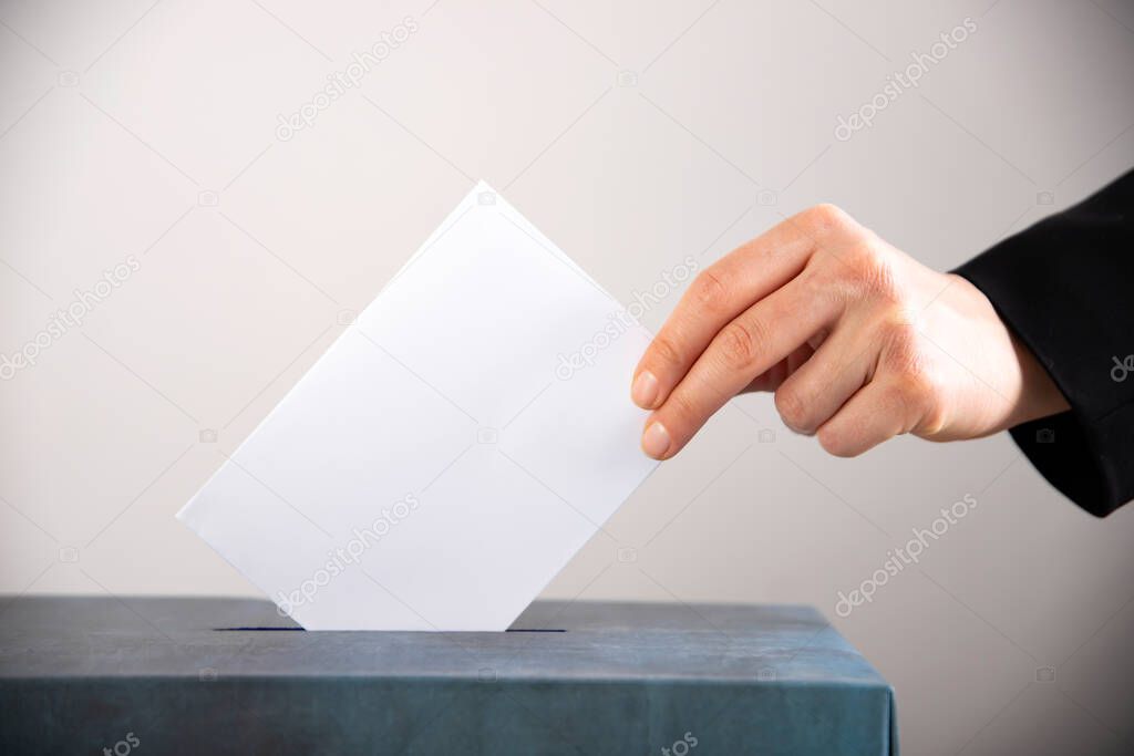 Hand of a voter putting vote in the ballot box. Election concept.