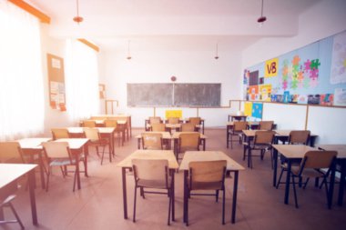 Okul konseptine geri dönelim. Sandalyeleri, masaları ve tahtası olan güneşli sınıfın bulanık görüntüsü.