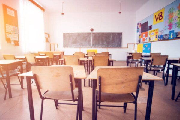 Back to school concept. Blurred view of sunny classroom with chairs, tables and blackboard.