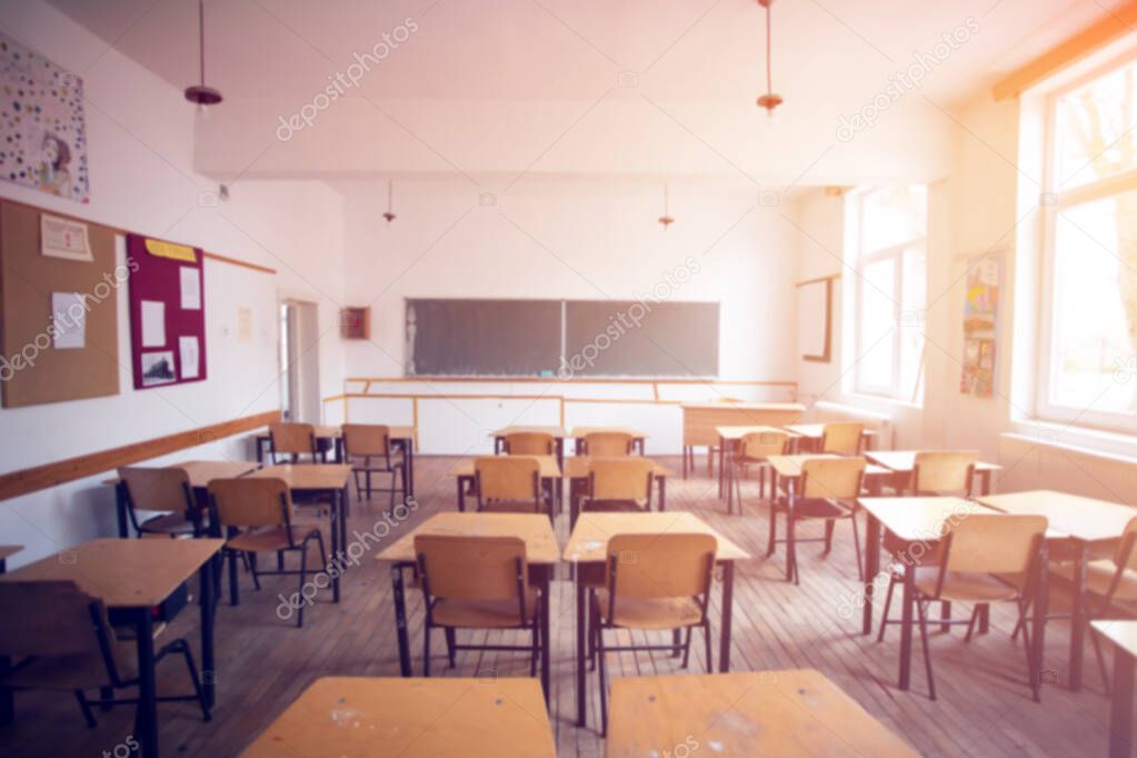 Back to school concept. Blurred view of sunny classroom with chairs, tables and blackboard.