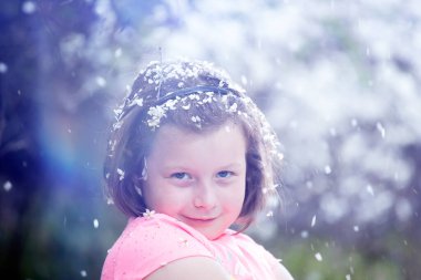 Çiçek açan ağaçların altında, bahçedeki sevimli küçük kız. Bahar taçyaprağı yağmuru.