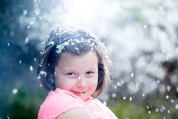可爱的小女孩在花园里 在开花的树下 春花瓣的雨 — 图库照片