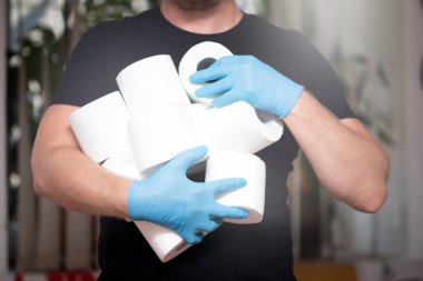 İnsanlar koronavirüs salgınından dolayı evdeki karantina için tuvalet kağıdı stokluyorlar. Adamın elinde bir sürü tuvalet kağıdı var..